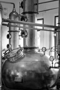 Black and white image of large industrial distillery equipment indoors.