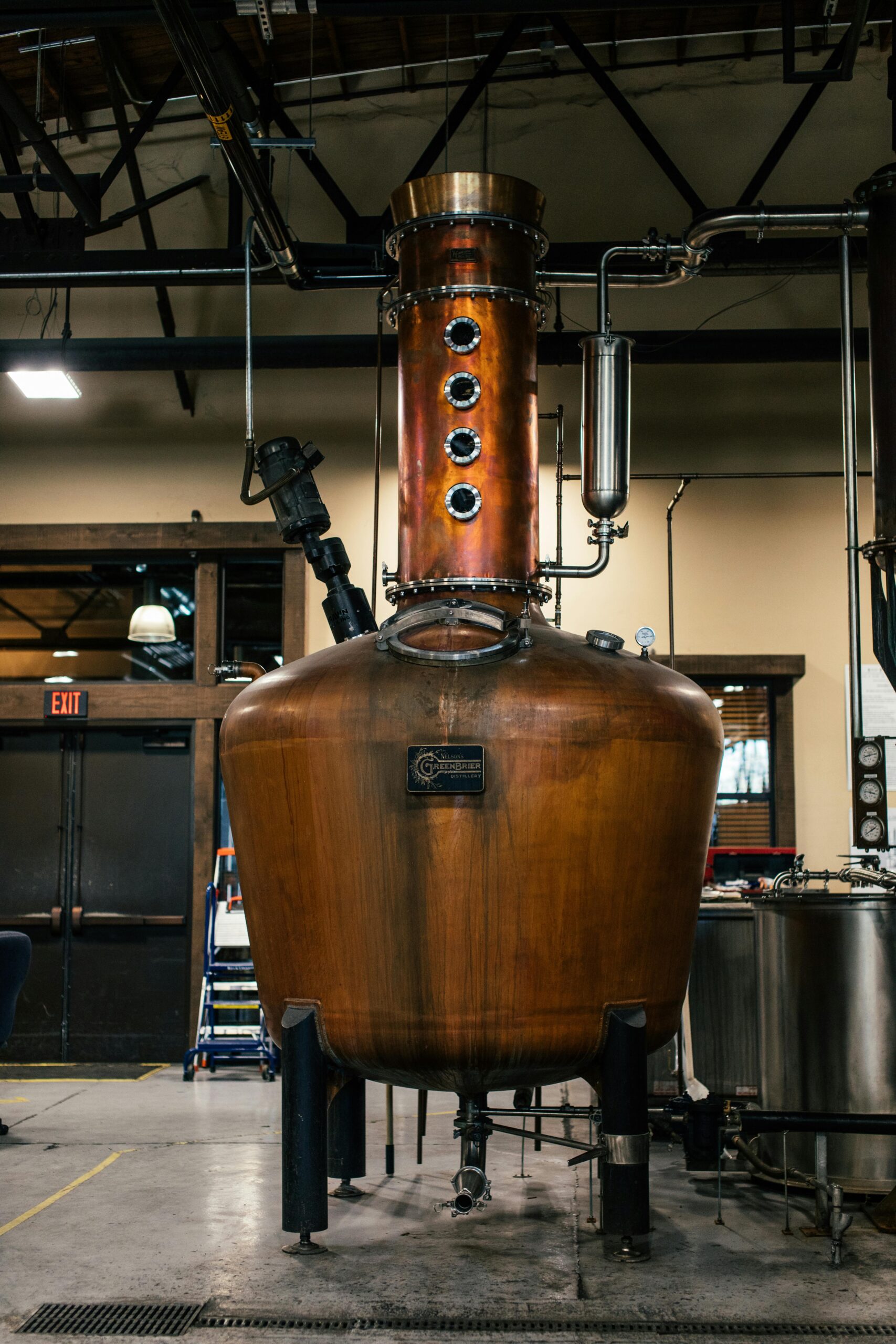 A copper distillation apparatus in an indoor industrial setting, showcasing brewery equipment.