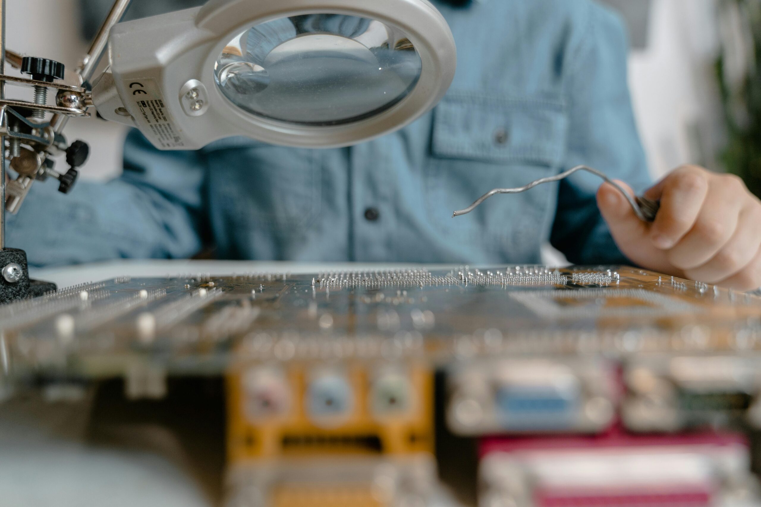 A detailed view of electronic circuit inspection using a magnifying glass and tools.
