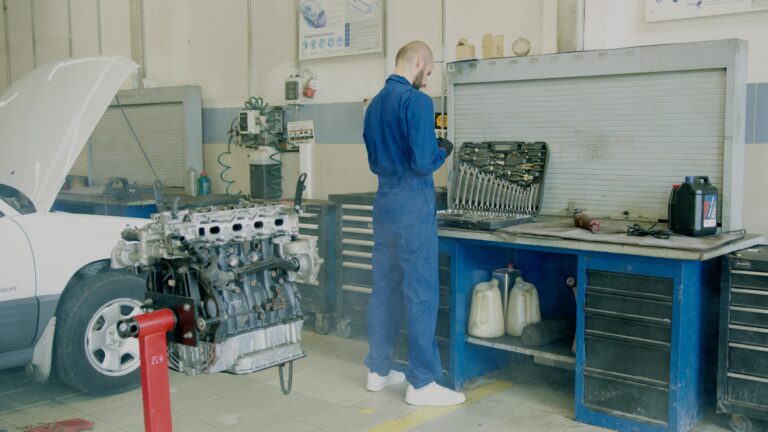 Mechanic in blue coveralls working on car engine in auto repair shop.